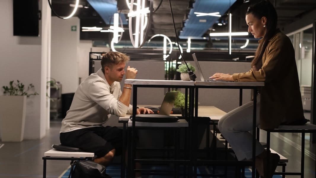 Zwei Menschen arbeiten mit Laptops an einem Hochtisch auf der Community-Fläche im MerkurOffice