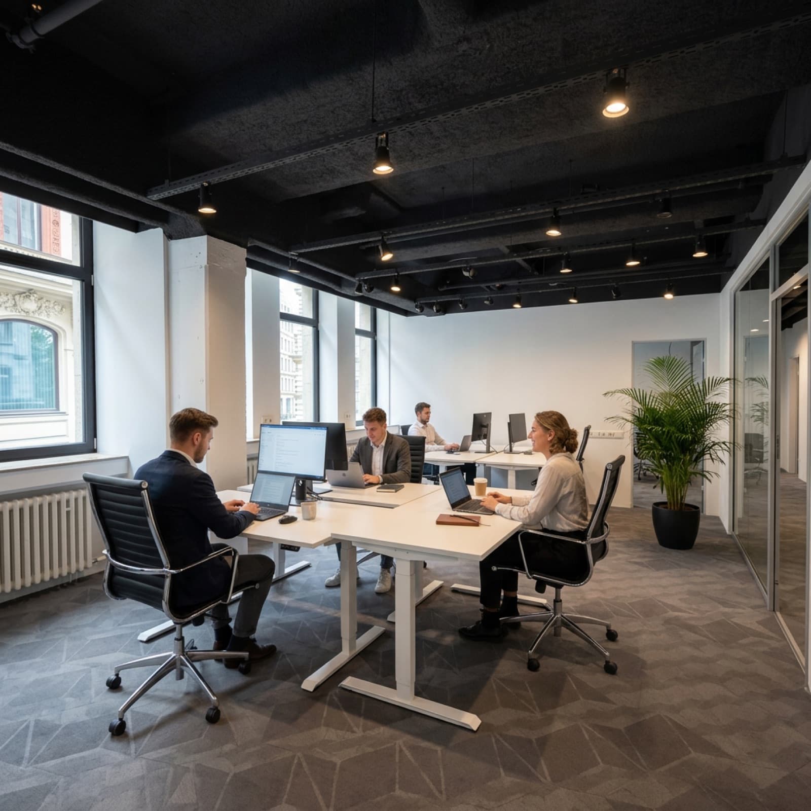 Helles Büro mit mehreren höhenverstellbaren Schreibtischen und Glastrennwand