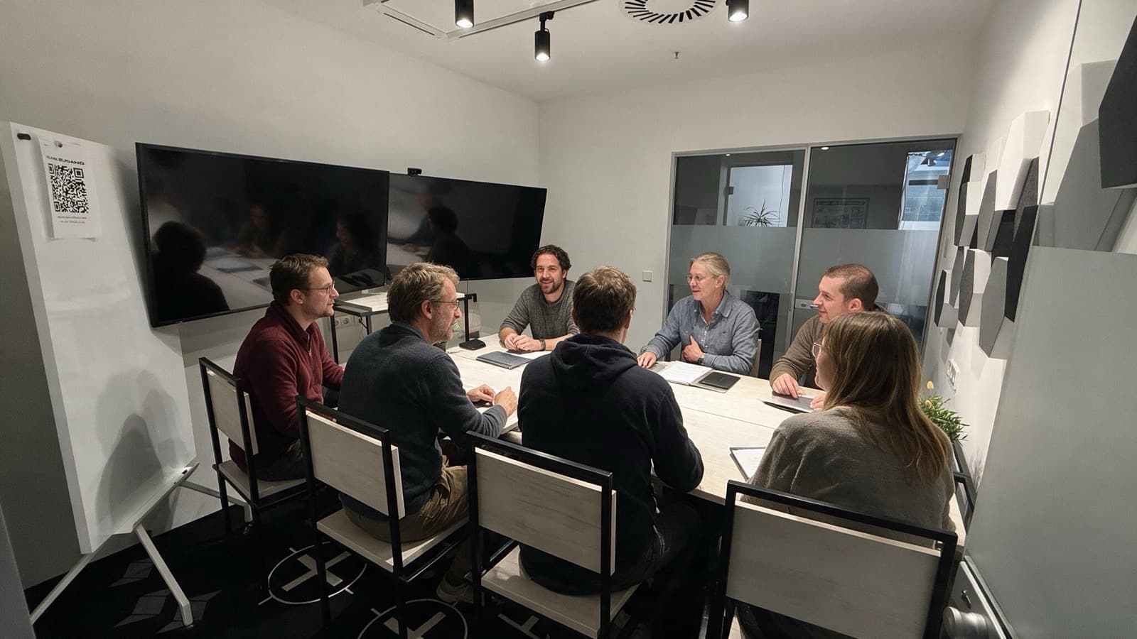 Besetzte Besprechung im Meetingraum L-CM 01, zwei Bildschirme an der Wand